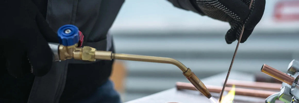 Person lötet Kupferrohre mit Gasbrenner.